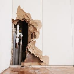 Damaged wall exposing burst water pipes after flood.
